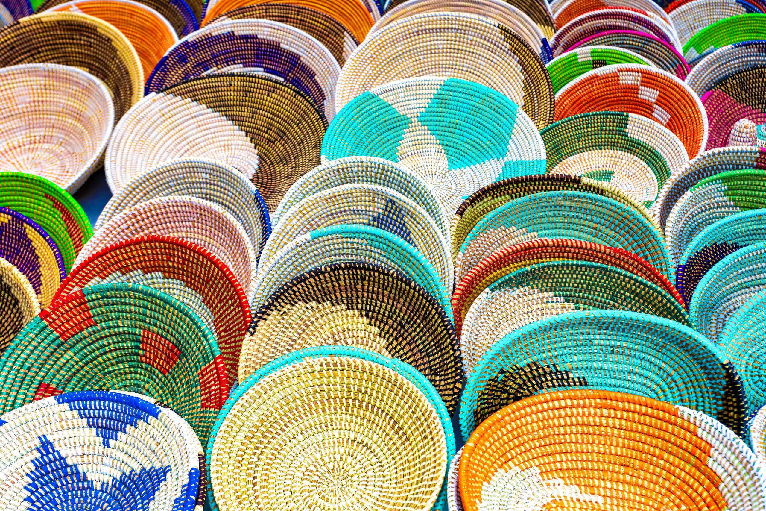 Ensemble de paniers tressés colorés exposés à la verticale, aux motifs géométriques variés, présentés sur un marché artisanal.