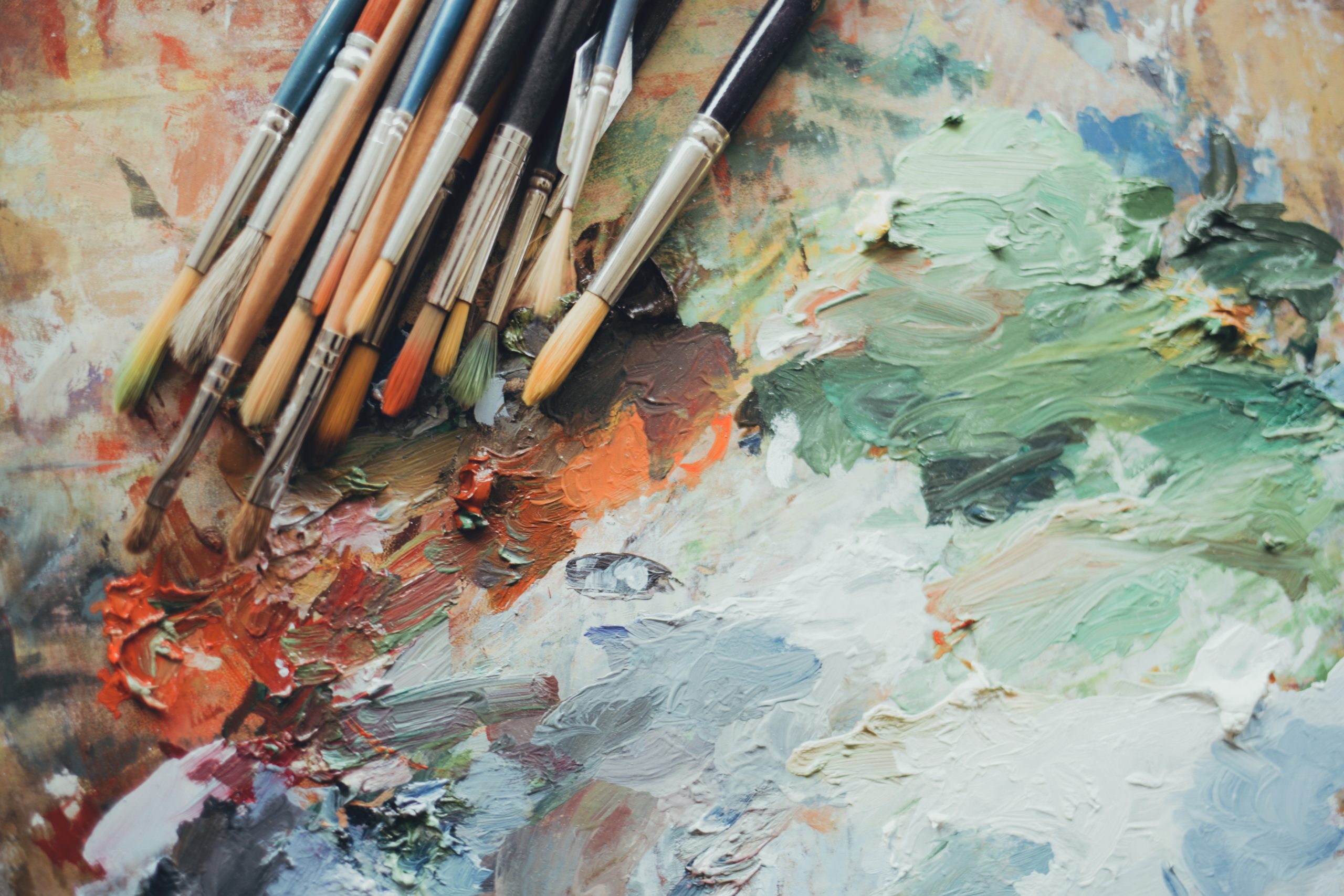 Palette de peinture avec plusieurs pinceaux utilisés, posés sur des mélanges épais de peinture à l’huile dans des tons verts, rouges, blancs et bleus.